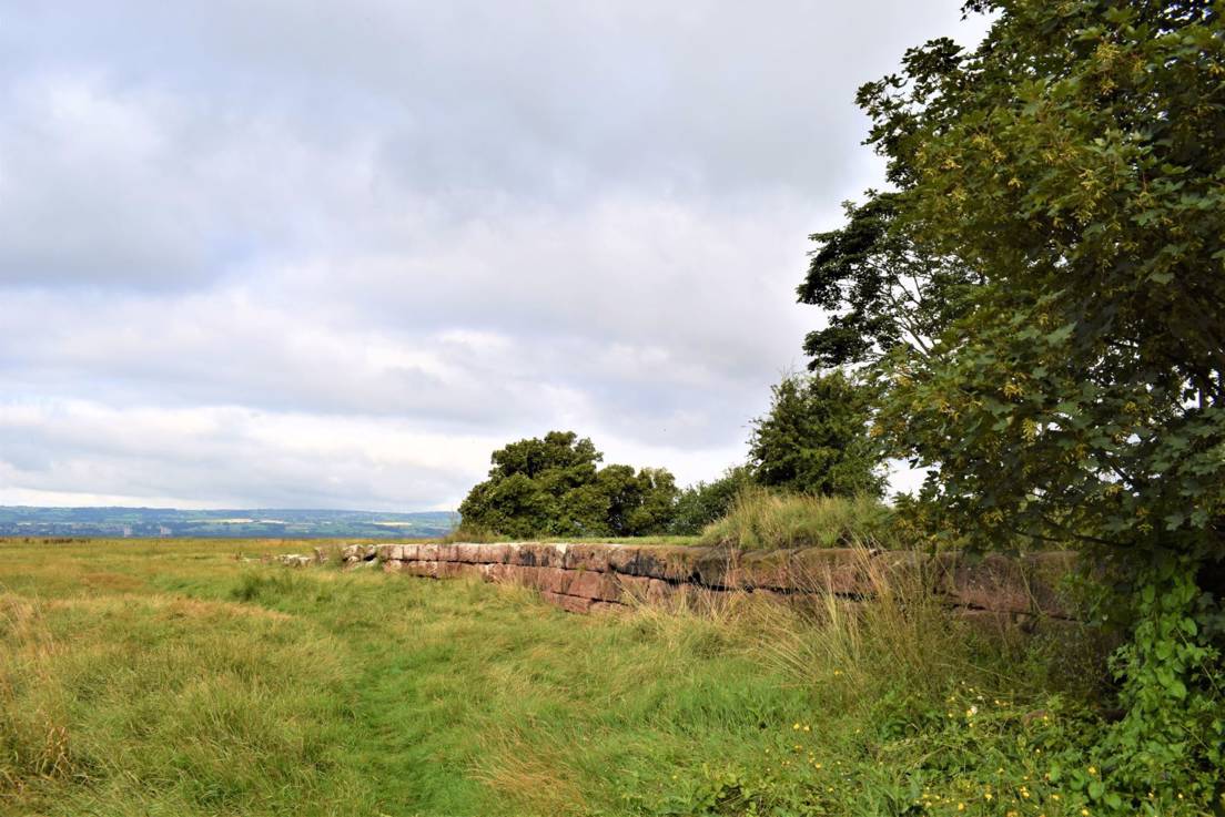 Sandstone blocks of former quay running out into marshland with the hills of North Wales in the distance across the River Dee